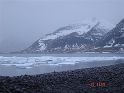 vík með hafís, snjór í fjöllum handan víkurinnar